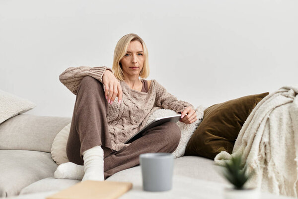 Блондинка расслабляется на удобном диване, погружается в книгу, одетая в теплую, уютную одежду.