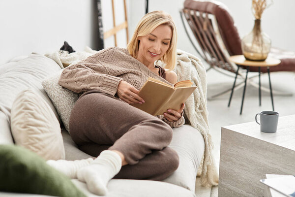 A blonde woman unwinds in her comfortable outfit while reading in her inviting home.
