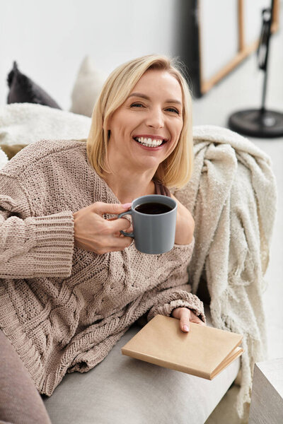 Blonde woman enjoys a warm drink while relaxing in her cozy apartment, embracing slow living.