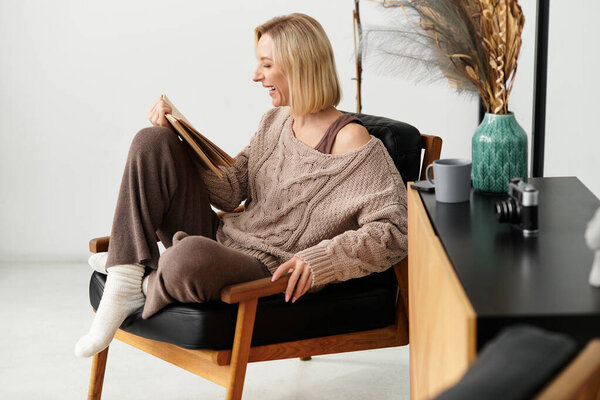 Blonde woman enjoys a quiet afternoon reading in her modern, cozy apartment, embracing self-care.