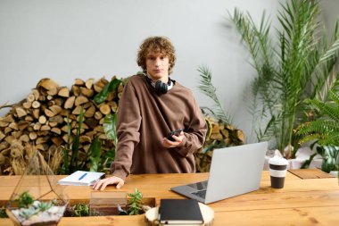 Kıvırcık saçlı genç bir adam işine odaklanırken etrafı bitkiler ve ahşap dekorlarla çevrili..