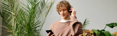 Yaratıcı genç adam dinlendirici bir atmosferde bitkilerle çevrili telefonuyla müzik dinliyor..