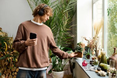 Kapalı bir alanda, genç bir adam kulaklıkla müzik dinlerken yeşil bitkilere hayrandır..