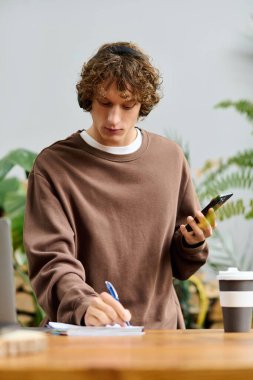 Genç adam notlar alırken yaratıcı düşünüyor ve canlı bir yerde akıllı telefon kullanıyor..