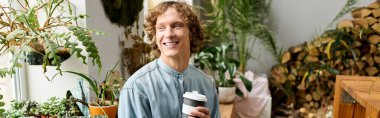 Genç adam, parlak, canlı bir odada çeşitli bitkilerin arasında bir fincan kahve tutarken gülümsüyor.