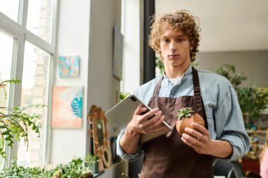Genç bir adam yeşil alanla çevrili küçük bir bitki ve tablet tutuyor..