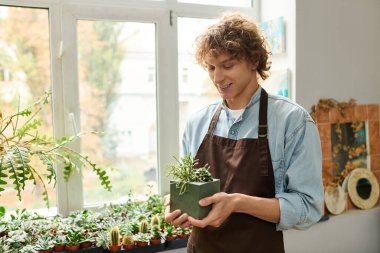 Genç bir adam elinde canlı yeşilliklerle çevrili küçük bir bitkiyi tutarken gülümsüyor..