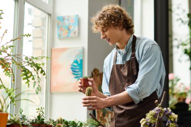 Genç bir adam dikkatli bir şekilde bitkilerle dolu canlı bir bahçede küçük bir kaktüsü sular..