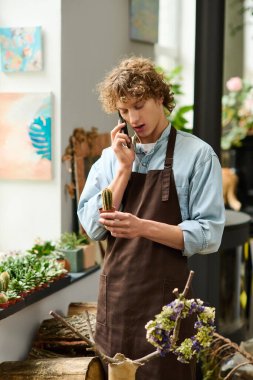 Genç yaratıcı bir adam telefonuyla konuşuyor. Etrafı yeşilliklerle çevrili bir kaktüsü dikkatle tutuyor..