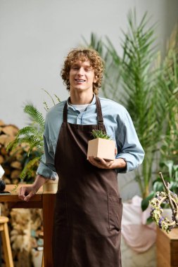 Genç bir adam küçük bir bitkiyi sıcacık, bitki dolu bir stüdyoda tutarken gülümsüyor..