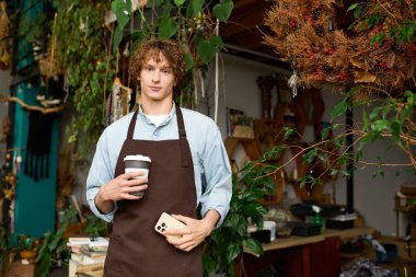 Genç bir adam canlı bir çalışma alanında elinde yeşil bir fincanla duruyor..
