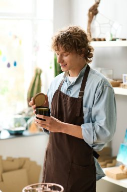 Kıvırcık saçlı genç adam yaratıcı çalışma alanında bir kap açarken gülümsüyor..