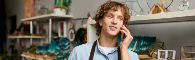 Etrafı sanatsal dekor ve el sanatları ile çevrili genç adam telefonda konuşuyor..