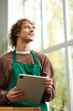 Kıvırcık saçlı genç bir adam tablet kullanırken neşeli bir atmosferden zevk alır..