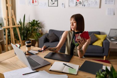 Genç kadın, canlı bir çalışma alanında renkli materyalleri ve dijital araçları dengeleyerek evde tasarımlar yapıyor..