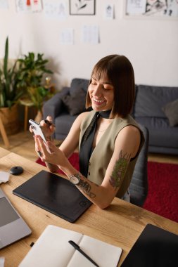 Genç bir kadın, yaratıcı aletlerle çevrili, rahat bir iş yerinde telefonunu kullanırken gülümsüyor..