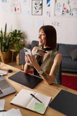 Genç yaratıcı kadın evde sanatla çevrili akıllı telefonuyla konuşurken gülümsüyor..