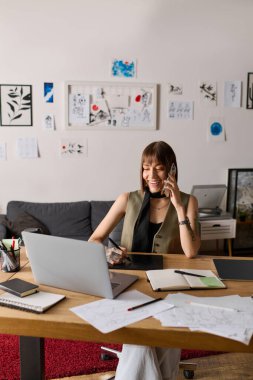 Genç bir kadın telefon konuşmasının keyfini çıkarırken ev ofisinde yaratıcı işler yapıyor..