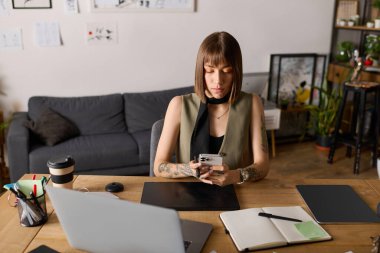 Genç bir kadın evinde bir proje üzerinde çalışıyor, akıllı telefonu ve not defterine odaklanıyor..
