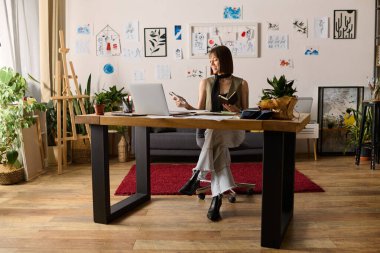 Genç bir kadın sanat eserleri ve yeşilliklerle çevrili, ev stüdyosunda sanatsal işler yapıyor..