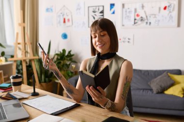 Genç bir kadın evde yaratıcı vakit geçirmeyi sever. Etrafı sanatla çevriliyken fikirleri not alır..