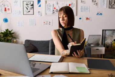 Genç bir kadın, rahat ofisindeki yaratıcı düşüncelerini yansıtan defterine odaklanıyor..