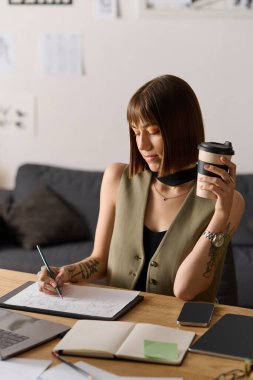 Evinde genç bir kadın yaratıcı fikirler çizerken kahvesini yudumluyor..