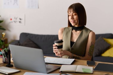 Genç kadın masasında oturuyor, kahvesini yudumluyor ve evde yaratıcı projeler üzerinde çalışıyor..