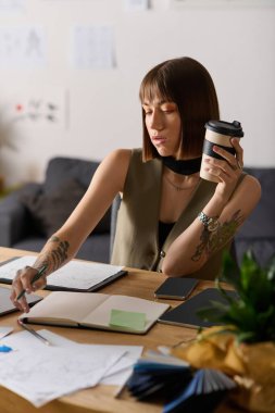 Genç kadın evde yaratıcılığına odaklanmış, ilham almak için eskiz çiziyor ve kahvesini yudumluyor..