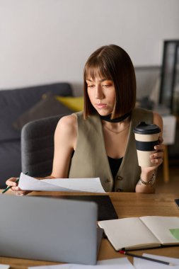 Genç bir kadın içeride bir fincan kahvenin tadını çıkarırken masasındaki belgeleri inceliyor..