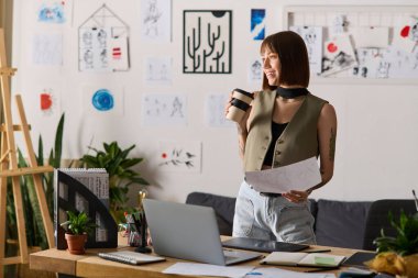 Evde, yaratıcı genç bir kadın sanatsal çizimlerini ve planlarını incelerken kahvenin tadını çıkarıyor..