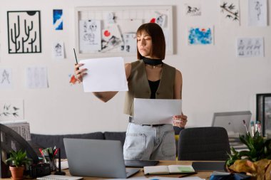 Genç bir kadın, parlak ve modern bir ev ofisinde dururken sanat eserlerini inceliyor..