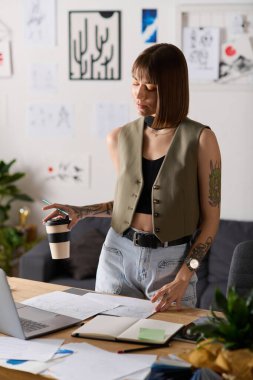 Genç bir kadın evde yaratıcı işler yapıyor, elinde kahve tutuyor ve etrafı sanatsal malzemelerle çevrili..