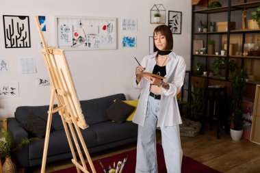 Genç bir kadın oturma odasında canlı bir dekorla dolaşırken tuvale resim yapıyor..