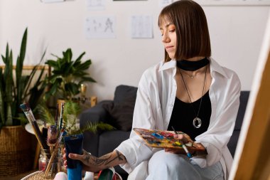 Genç bir kadın, ilham ve bitkilerle dolu canlı bir ev stüdyosunda tutkuyla sanat eseri yapıyor..