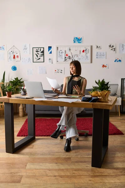 Genç, yaratıcı bir kadın, rahat bir iş yerinde sanat eserlerini incelerken gülümsüyor..