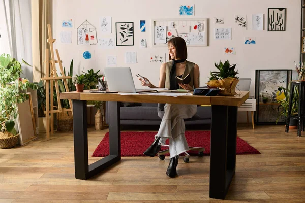 Genç bir kadın sanat eserleri ve yeşilliklerle çevrili, ev stüdyosunda sanatsal işler yapıyor..