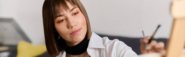 Young woman with short hair immerses herself in painting at home, showcasing her creativity.