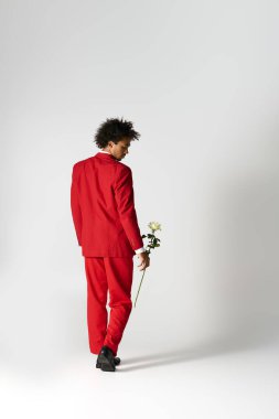 Kırmızı elbiseli genç, yakışıklı bir adam zarif bir şekilde yürür, elinde beyaz bir gül tutarken yüzünü çevirir..