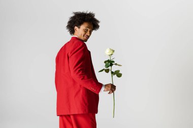 Kırmızı takım elbiseli şık bir genç beyaz bir gül tutarken sırıtıyor, zarafet saçıyor..