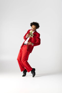 Parlak kırmızı takım elbiseli genç, yakışıklı adam bir gülle dans ediyor, neşe ve zarafet ifade ediyor..