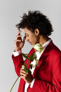 Zarif kırmızı takım elbiseli genç bir adam derin düşüncelere dalmış beyaz bir gül tutuyor..