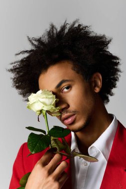 Kırmızı elbiseli yakışıklı genç adam beyaz bir gül tutuyor, kendine güveni tam..