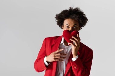 Şık kırmızı bir ceket giymiş genç yakışıklı bir adam yüzünü bir kalbin arkasına saklar..