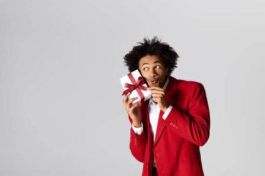 Kırmızı takım elbiseli yakışıklı bir genç elinde bir hediyeyle yaramazca gülümsüyor..