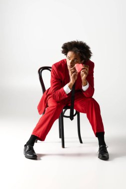 Kalın kırmızı elbiseli şık bir genç adam kendine güvenerek oturur ve elinde bir kalp taşır..