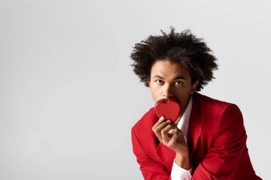 Şık bir genç adam kalp şeklinde bir kutuyla neşe içinde poz verir..