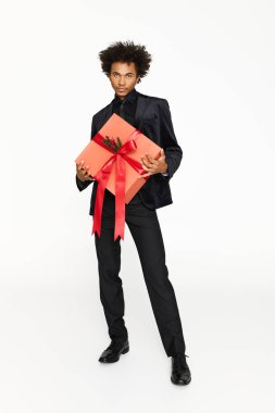 Zarif giyinmiş şık bir genç adam bir partide neşeli bir tebessümle parlak bir hediye tutar..