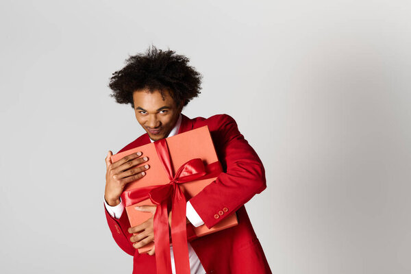 A young man in a stylish red suit smiles while holding festive gifts tied with ribbons.