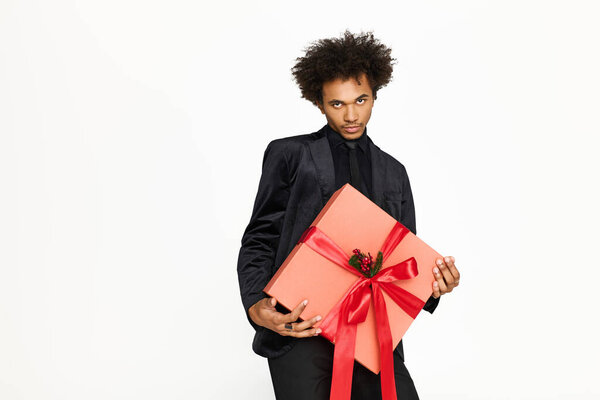 A young, handsome man wearing elegant attire holds a beautifully wrapped gift with a festive ribbon.